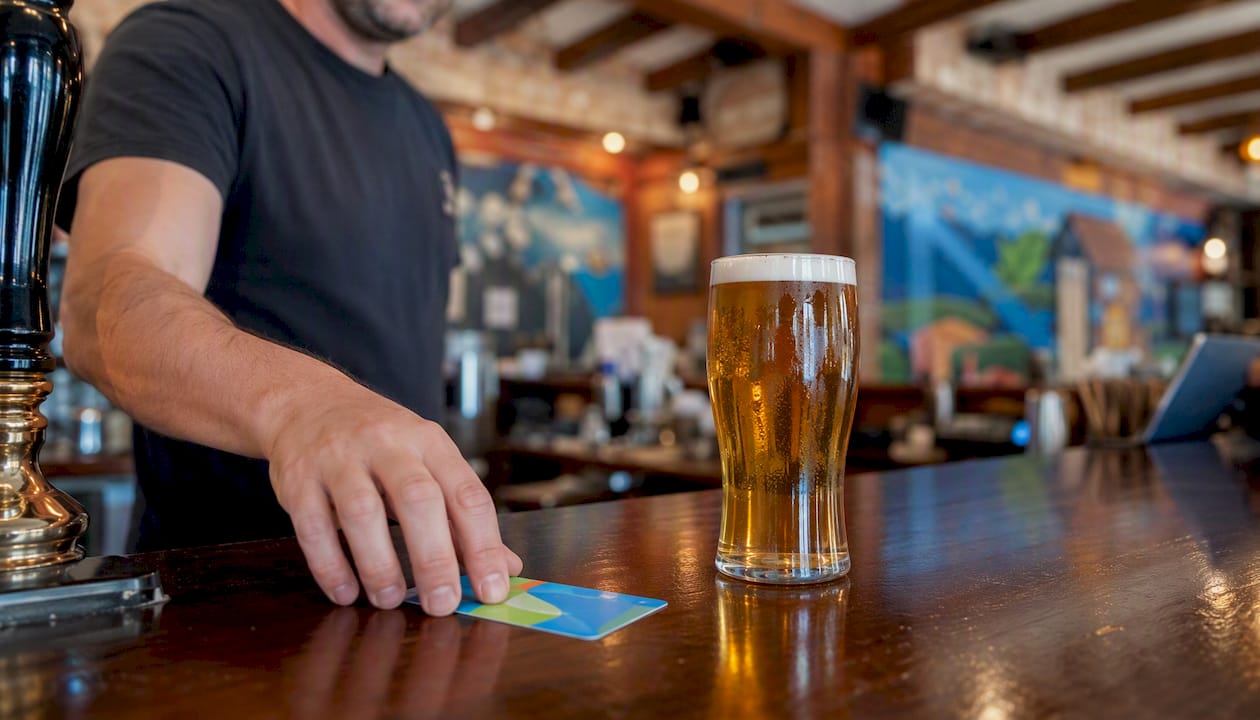 Hand sliding loyalty card next to pint in pub