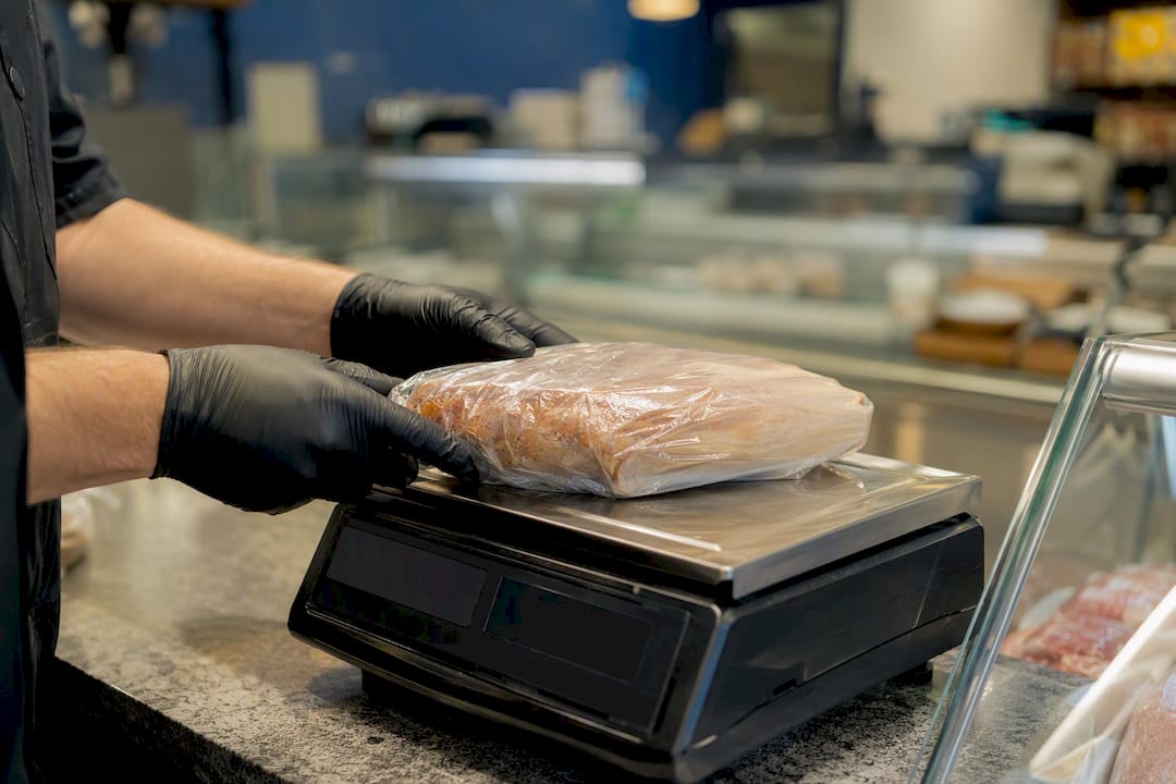 Hands weighing packaged deli item on scale